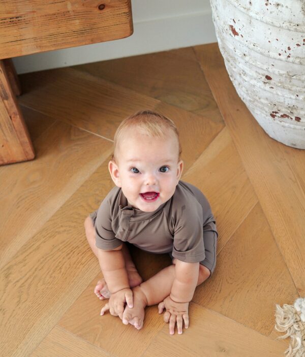 A baby is sitting on a Zimmi Onesie - Tort floor.